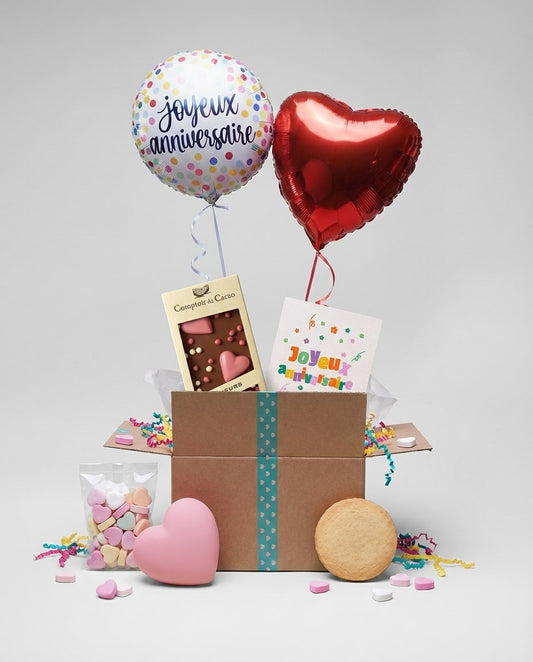 Coffret surprise ouvert avec deux ballons hélium et carte d’anniversaire dans un intérieur chaleureux