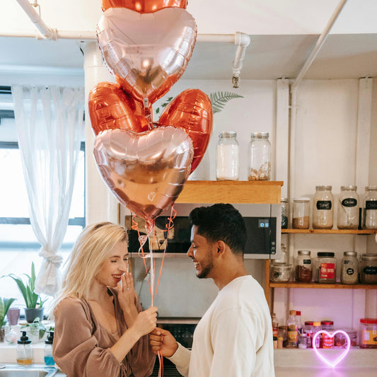 Un couple heureux se regarde en souriant, entouré de ballons à hélium colorés. Leur bonheur éclate à travers leurs sourires radieux, créant une atmosphère de joie et de célébration.