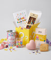Coffret cadeau anniversaire ouvert avec boîte surprise jaune, chocolats et biscuits