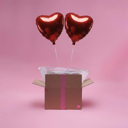 Deux ballons cœur rouges gonflés à l’hélium sortant d’une box cadeau sur fond rose