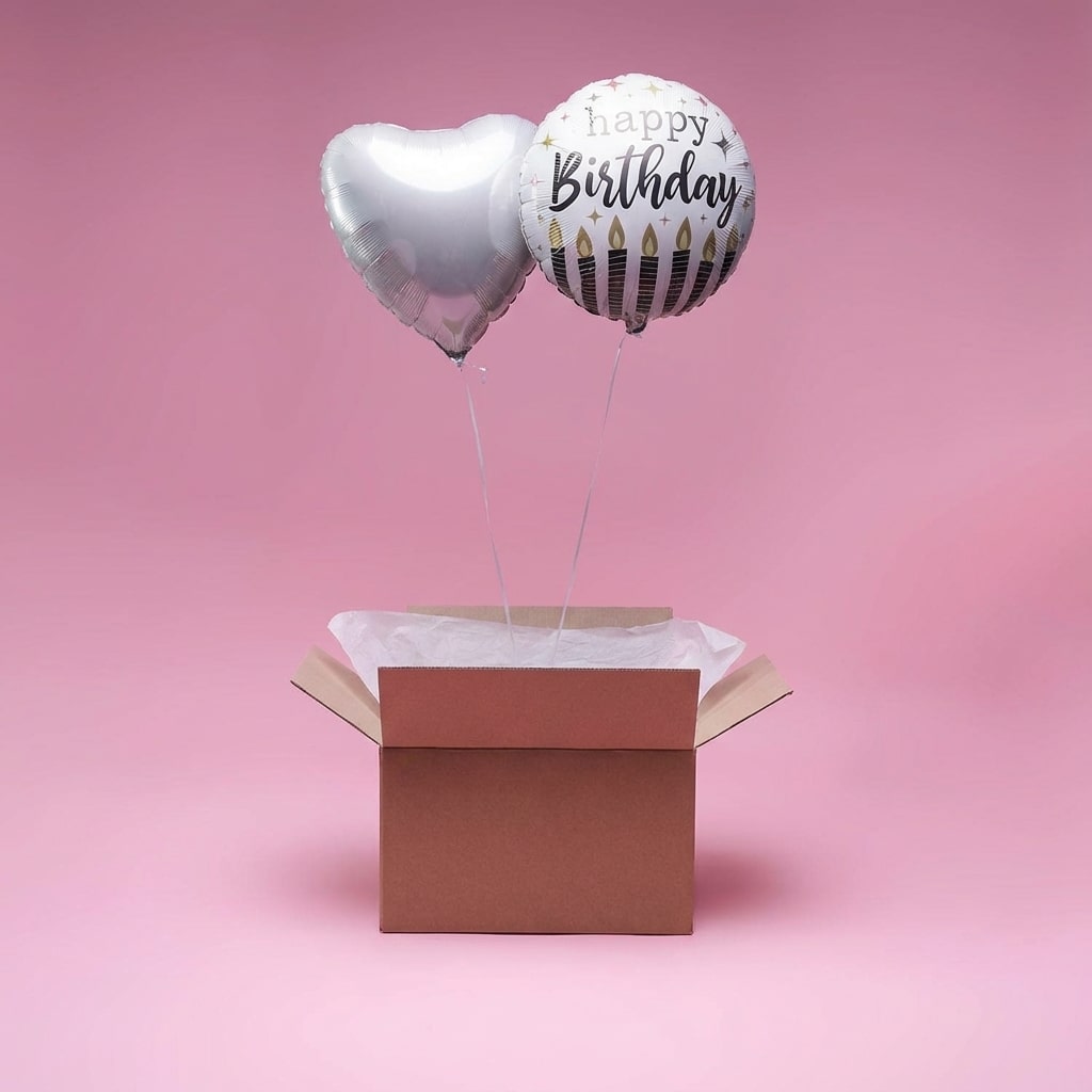 Ballons argent en forme de cœur et ballon rond Happy Birthday dans une box cadeau sur fond rose