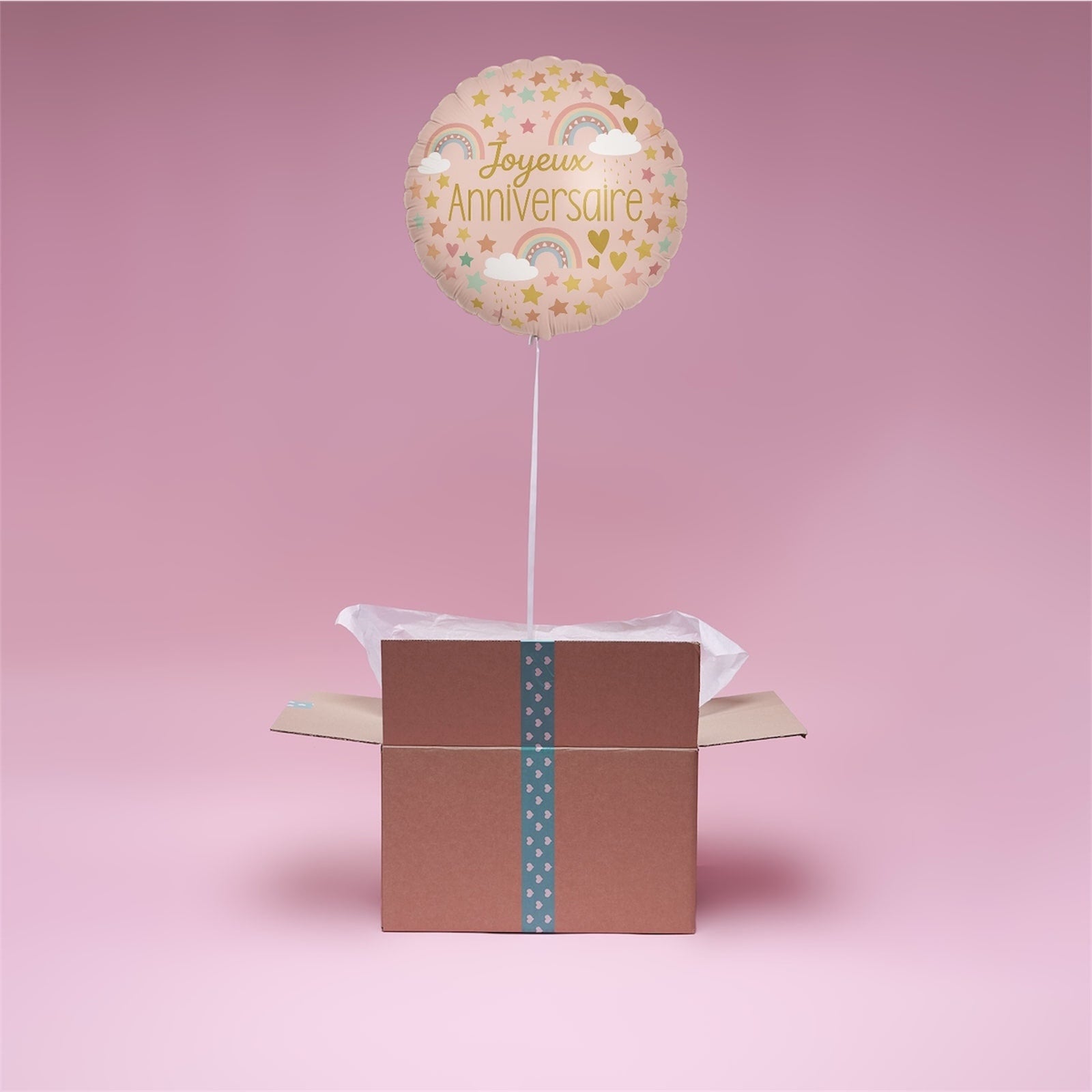 Ballon Arc-en-Ciel Joyeux Anniversaire en hélium flottant au-dessus d’une box cadeau rose Lune des Cœur.