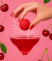 Bombe à cocktail cerise amande tenue au-dessus d’un verre rouge