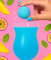 Bombe à cocktail tropicale bleue tenue au-dessus d’un verre, mangue et passion en décor