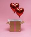 👉 Deux ballons cœur rouges gonflés à l’hélium sortant d’une box cadeau sur fond rose