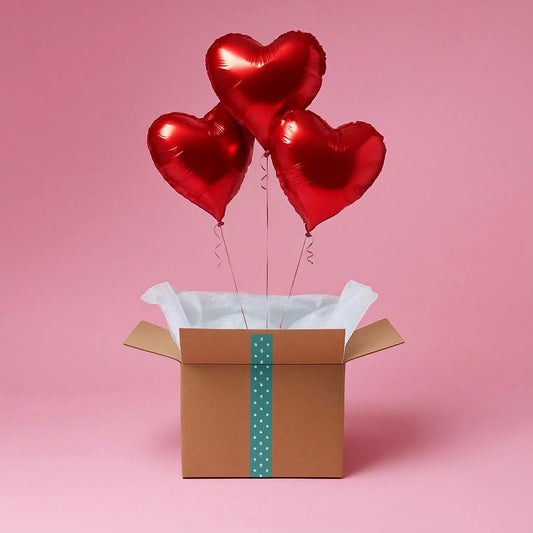 Trois ballons cœur rouges gonflés à l’hélium sortant d’une box cadeau sur fond rose.